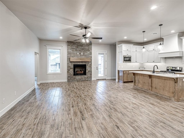 kitchen with white cabinetry, a large island with sink, custom range hood, pendant lighting, and stainless steel appliances