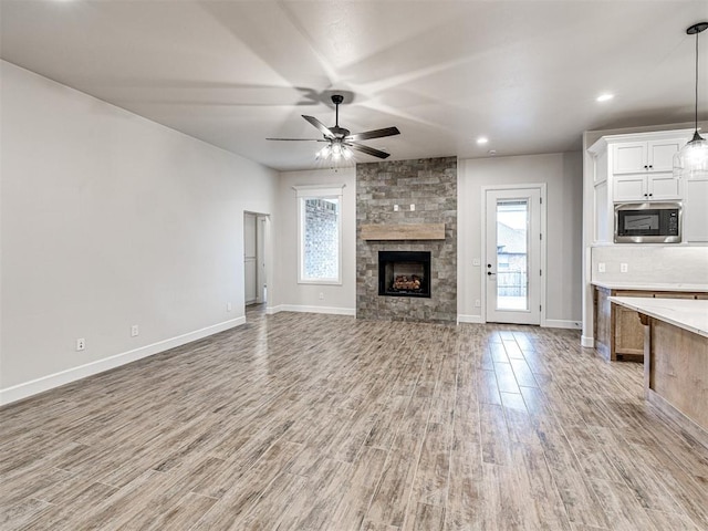 unfurnished living room with a stone fireplace, light hardwood / wood-style flooring, and ceiling fan