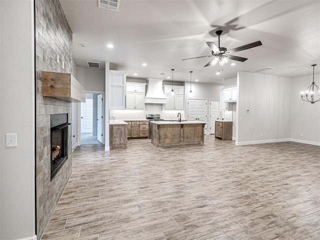 kitchen featuring white cabinetry, custom range hood, a center island with sink, and pendant lighting