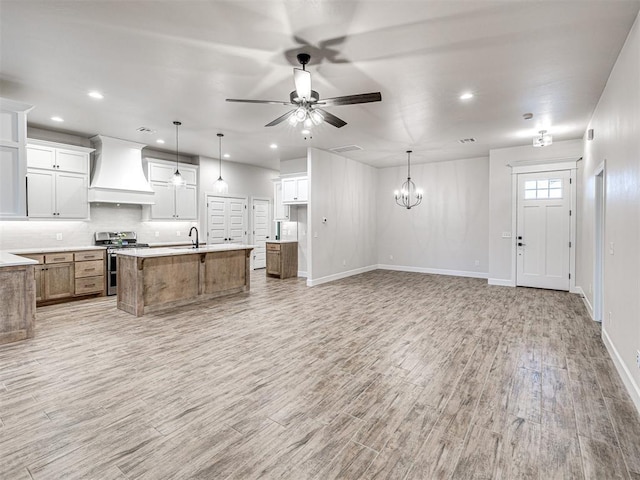 kitchen featuring white cabinets, range with two ovens, hanging light fixtures, a large island, and custom range hood