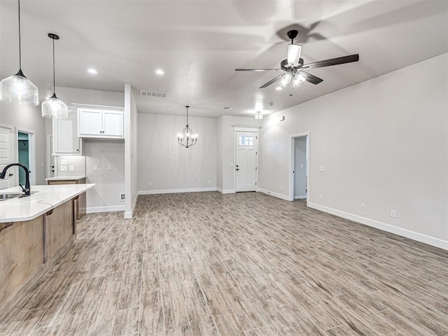 kitchen featuring pendant lighting, sink, light hardwood / wood-style flooring, white cabinetry, and ceiling fan with notable chandelier