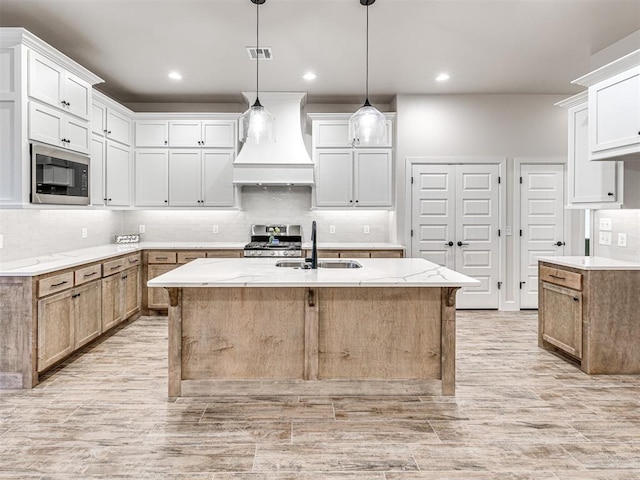 kitchen with built in microwave, white cabinetry, sink, custom range hood, and a center island with sink