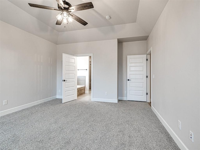 unfurnished bedroom featuring ensuite bathroom, vaulted ceiling, light carpet, a raised ceiling, and ceiling fan