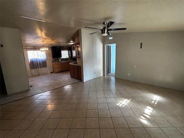 unfurnished living room with sink, ceiling fan with notable chandelier, a textured ceiling, and light tile patterned floors