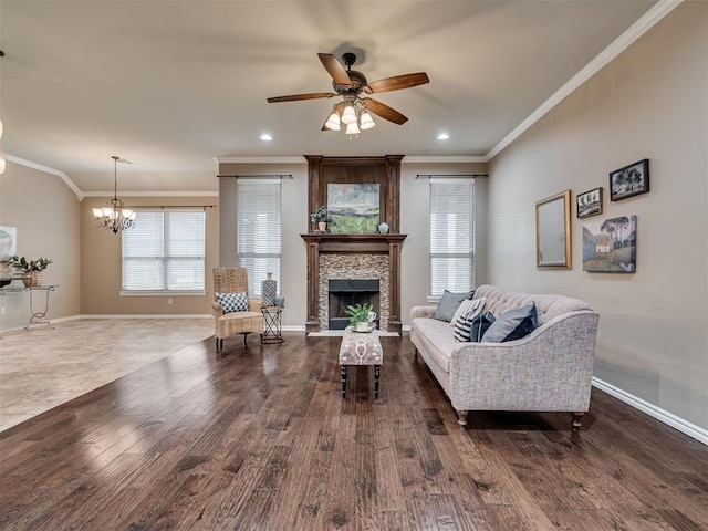 living room featuring ornamental molding, dark hardwood / wood-style flooring, ceiling fan with notable chandelier, and a stone fireplace