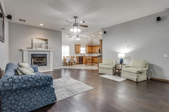 living room with ceiling fan, dark hardwood / wood-style floors, and a tiled fireplace