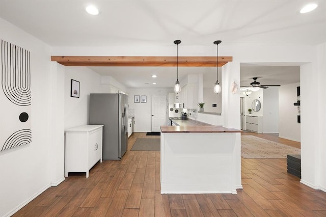 kitchen with dark hardwood / wood-style floors, white cabinets, stainless steel fridge, hanging light fixtures, and kitchen peninsula