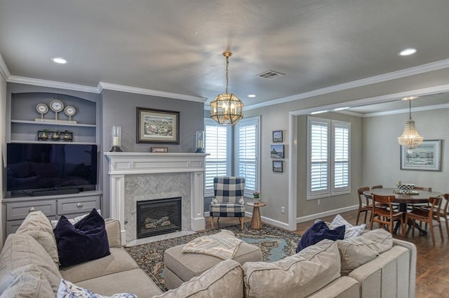 living room featuring crown molding, built in features, an inviting chandelier, a fireplace, and wood-type flooring