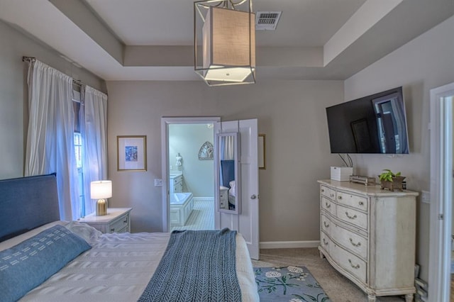 bedroom with a raised ceiling, ensuite bathroom, and light colored carpet