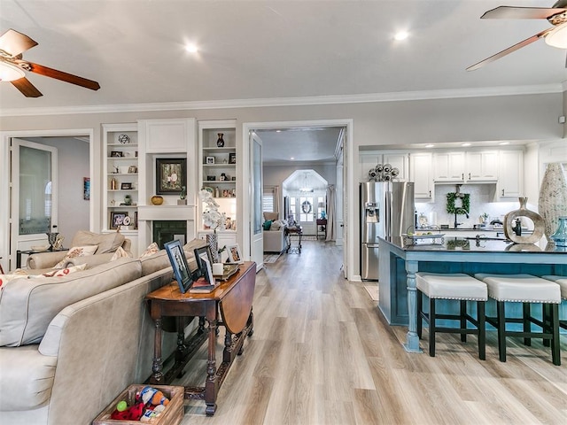 living room with crown molding, ceiling fan, and light wood-type flooring