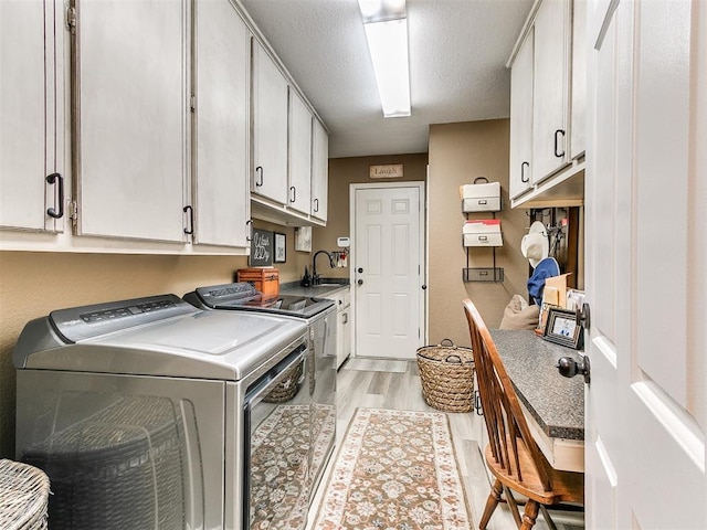 laundry area featuring sink, washing machine and dryer, cabinets, a textured ceiling, and light hardwood / wood-style floors