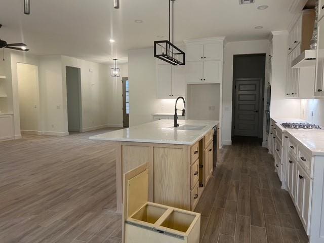 kitchen with white cabinetry, hanging light fixtures, a kitchen island with sink, dark wood-type flooring, and wall chimney range hood