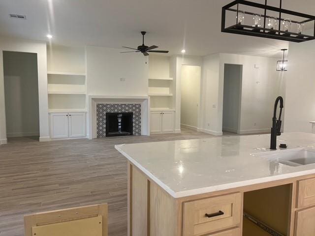 kitchen featuring a tile fireplace, sink, pendant lighting, and light brown cabinetry