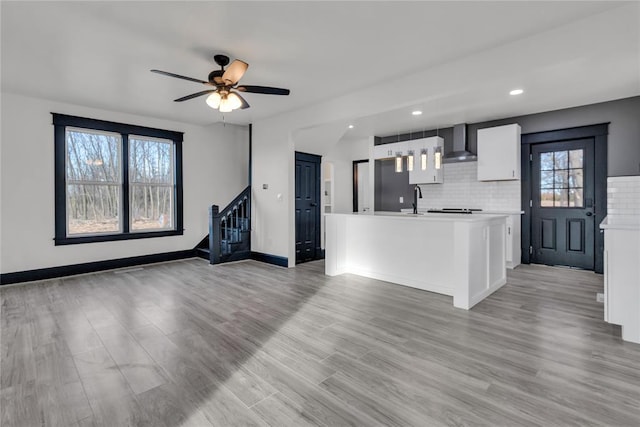 kitchen with white cabinetry, light wood-type flooring, an island with sink, decorative backsplash, and wall chimney range hood