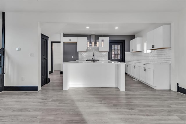 kitchen with tasteful backsplash, decorative light fixtures, light hardwood / wood-style flooring, an island with sink, and white cabinets