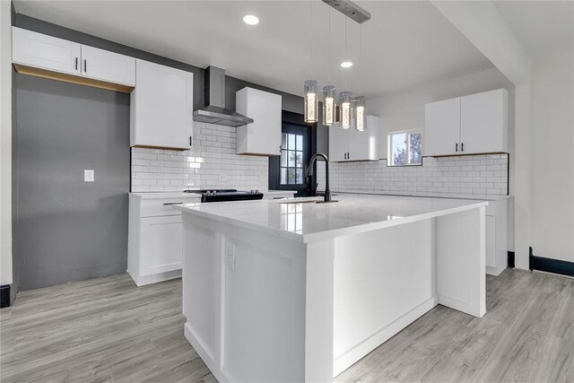 kitchen featuring white cabinetry, sink, pendant lighting, and wall chimney exhaust hood