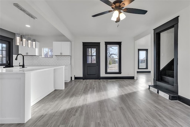 kitchen featuring decorative light fixtures, tasteful backsplash, white cabinetry, sink, and light wood-type flooring