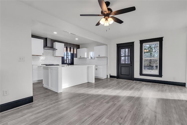 kitchen featuring white cabinetry, wall chimney range hood, hanging light fixtures, and a center island with sink