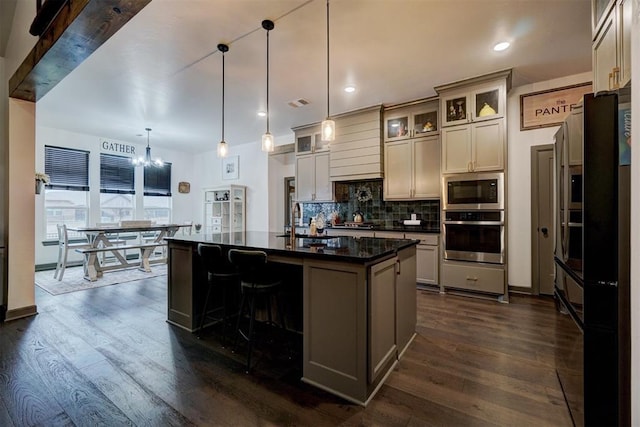 kitchen with dark hardwood / wood-style floors, tasteful backsplash, an island with sink, decorative light fixtures, and stainless steel oven