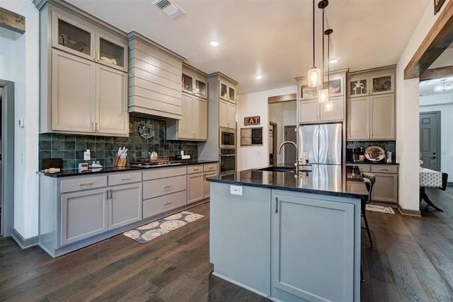 kitchen featuring dark wood-type flooring, sink, decorative light fixtures, an island with sink, and stainless steel appliances