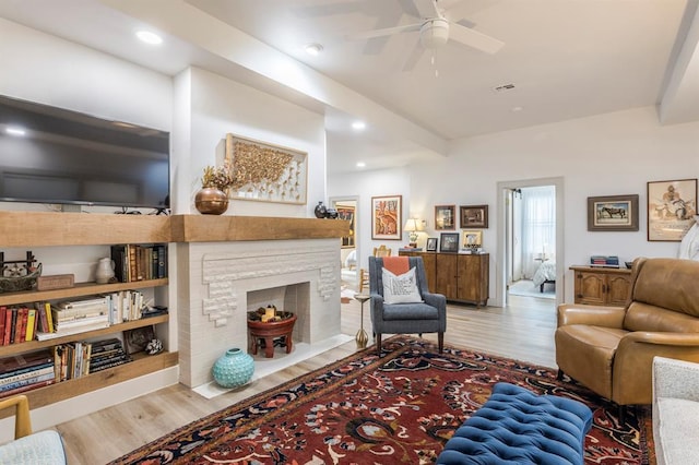 living room with ceiling fan, a stone fireplace, and light hardwood / wood-style floors