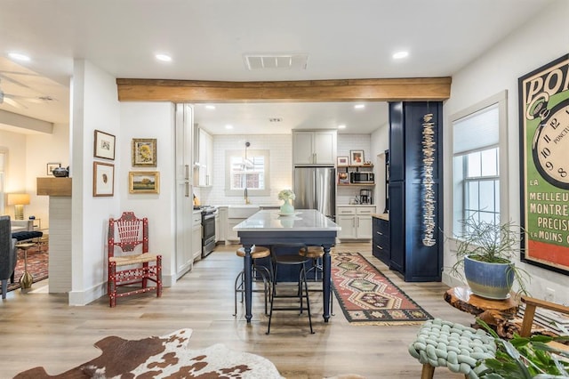 dining room featuring beamed ceiling, a healthy amount of sunlight, sink, and light hardwood / wood-style flooring