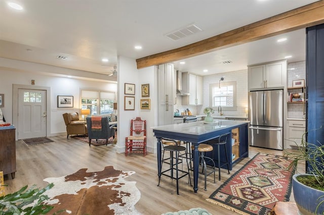 kitchen featuring a breakfast bar, white cabinetry, appliances with stainless steel finishes, beamed ceiling, and wall chimney range hood