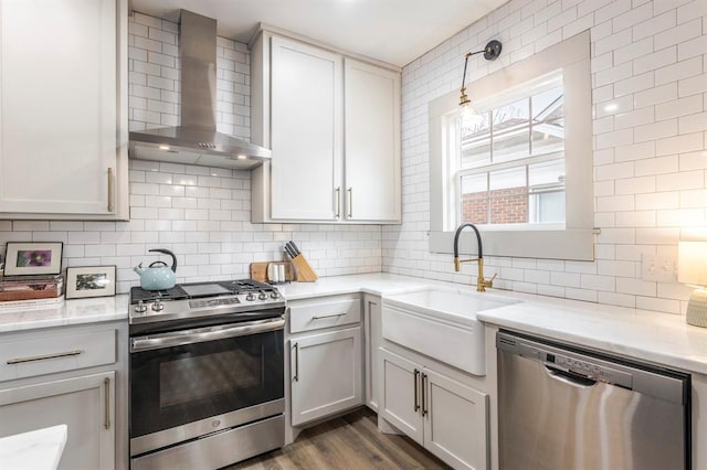 kitchen featuring appliances with stainless steel finishes, white cabinetry, sink, hanging light fixtures, and wall chimney exhaust hood