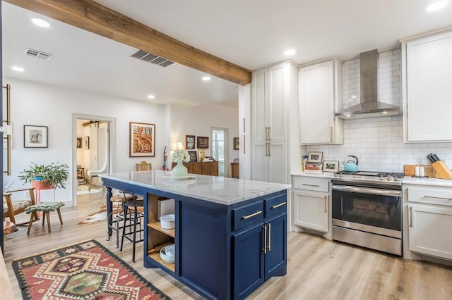 kitchen with wall chimney exhaust hood, white cabinets, blue cabinets, gas range, and beamed ceiling