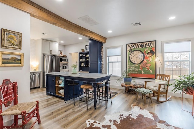 kitchen with light hardwood / wood-style flooring, a center island, beamed ceiling, and a kitchen bar