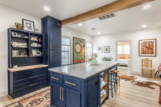 kitchen featuring blue cabinetry, a breakfast bar, beam ceiling, a center island, and light wood-type flooring