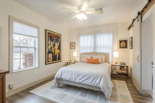 bedroom with ceiling fan, wood-type flooring, and a barn door