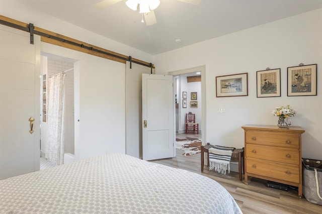 bedroom featuring ceiling fan, a barn door, and light wood-type flooring