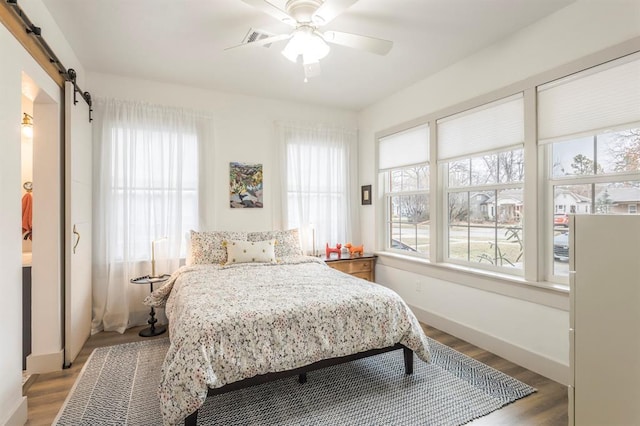 bedroom featuring multiple windows, wood-type flooring, a barn door, and ceiling fan