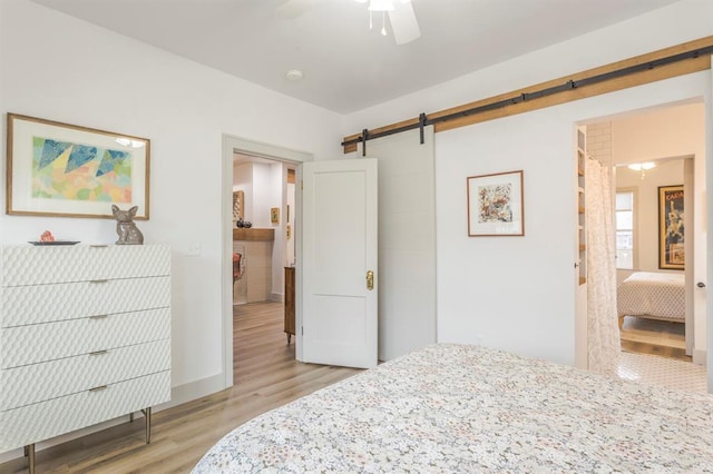 bedroom featuring ceiling fan, a barn door, and light hardwood / wood-style floors