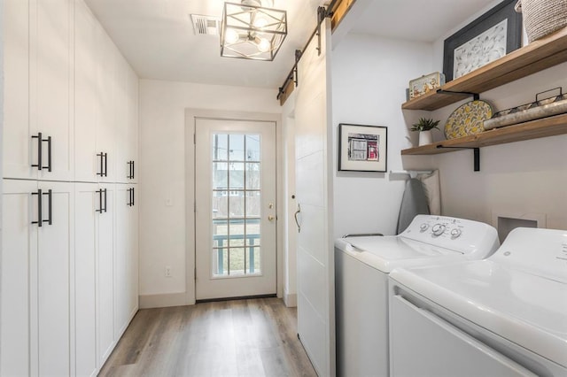 laundry room with washer and dryer, cabinets, a barn door, and light wood-type flooring