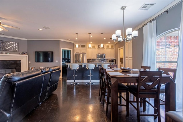 dining area with ceiling fan with notable chandelier, a fireplace, and ornamental molding