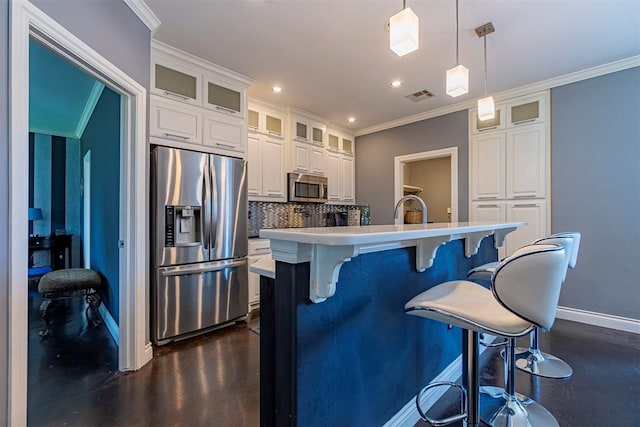 kitchen featuring white cabinetry, stainless steel appliances, ornamental molding, a center island with sink, and decorative light fixtures