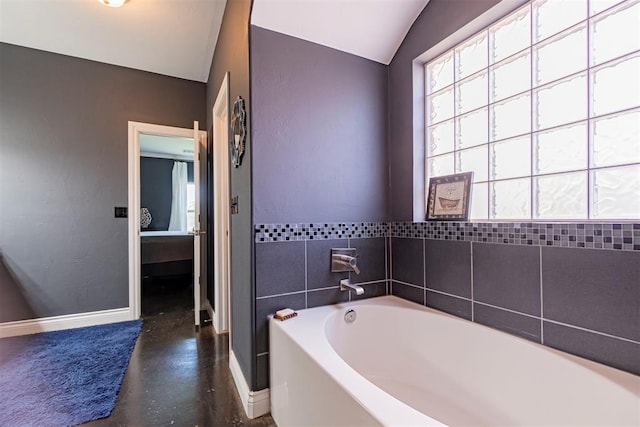 bathroom with a bath, concrete flooring, and vaulted ceiling