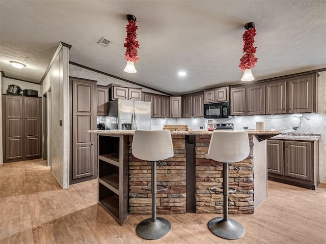 kitchen with stainless steel fridge with ice dispenser, light wood-style flooring, a breakfast bar area, a center island, and black microwave