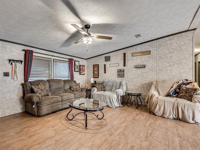 living room with a ceiling fan, a textured ceiling, ornamental molding, and wood finished floors