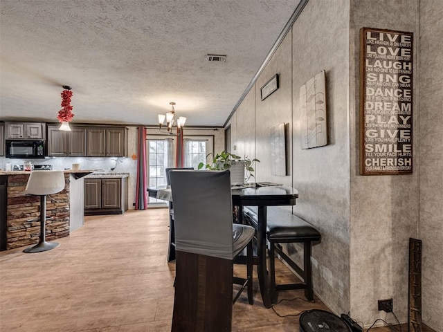 dining area featuring crown molding, visible vents, a textured ceiling, a chandelier, and light wood-type flooring