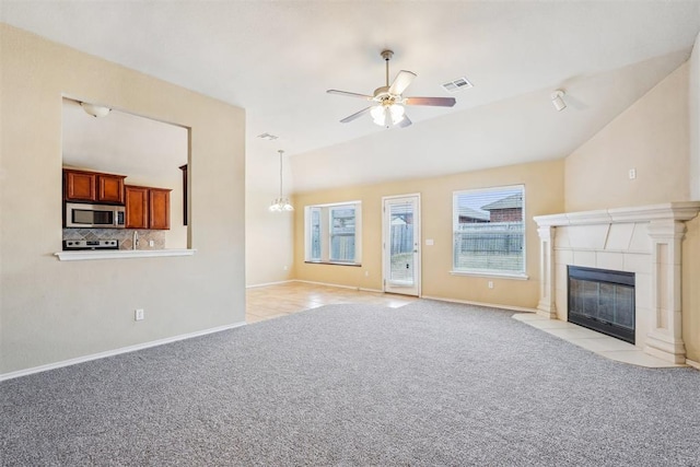 unfurnished living room with vaulted ceiling, light colored carpet, a tiled fireplace, and ceiling fan with notable chandelier