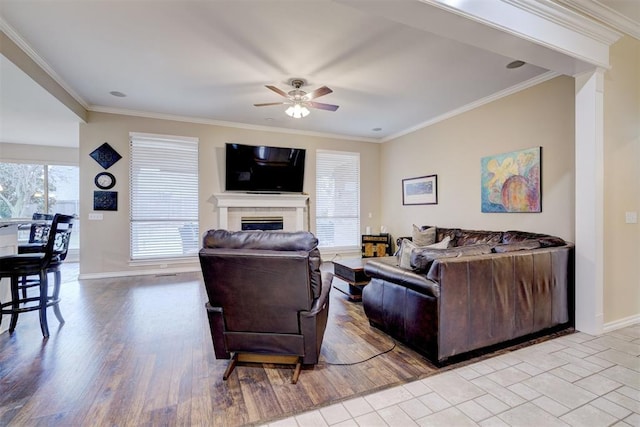 living room featuring crown molding, ceiling fan, a fireplace, and light wood-type flooring