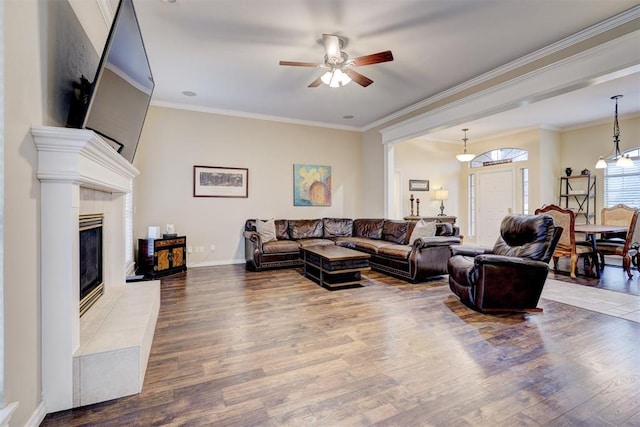 living room with hardwood / wood-style flooring, ceiling fan, ornamental molding, and a fireplace