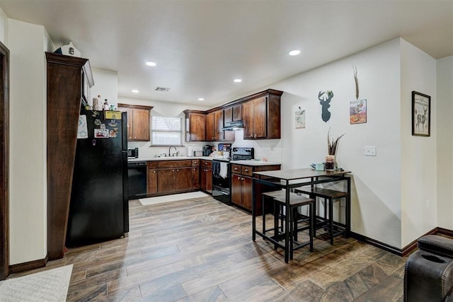 kitchen featuring dark brown cabinetry, sink, hardwood / wood-style floors, and black appliances