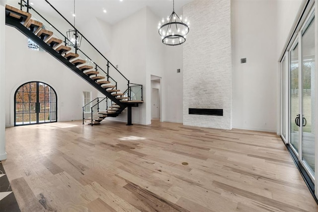 unfurnished living room featuring a stone fireplace, a wealth of natural light, a notable chandelier, and light hardwood / wood-style floors