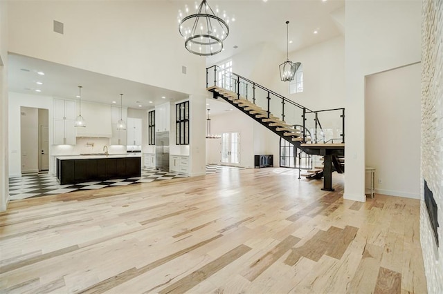 unfurnished living room featuring a towering ceiling, sink, a chandelier, and light hardwood / wood-style flooring