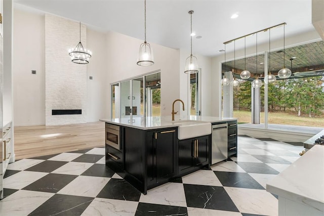 kitchen with sink, a large fireplace, hanging light fixtures, stainless steel appliances, and a center island with sink