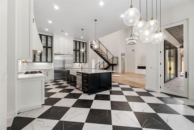 kitchen with pendant lighting, stainless steel appliances, white cabinets, and a center island with sink